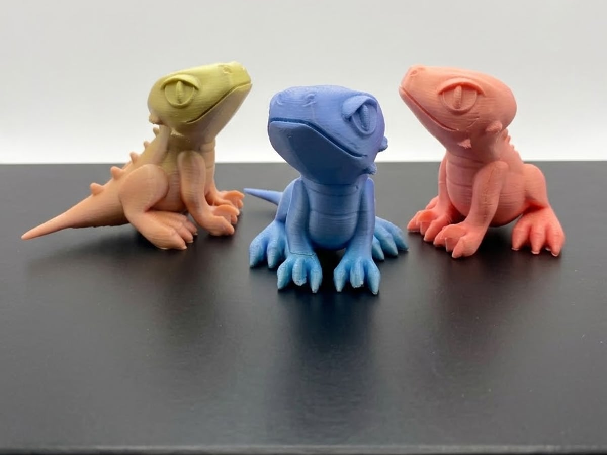 The same velociraptor printed three times, in yellow, blue and coral filament